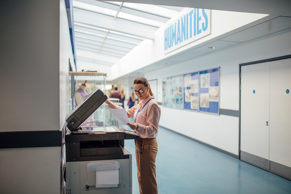 Teacher is printing off work sheets for her next lesson using the printer in the school hall. Managed print services concept.