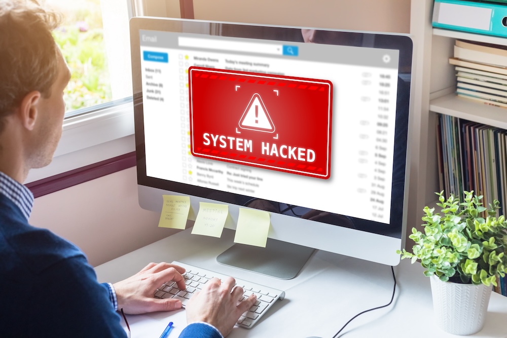 System hacked alert on computer screen after cyber attack on network. Cybersecurity vulnerability on internet, virus, data breach, malicious connection. Employee working in office.